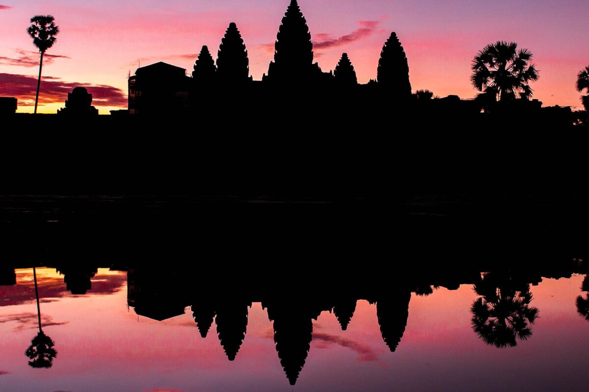 Angkor Wat silhouetted against a pink sunrise and reflected in the pond