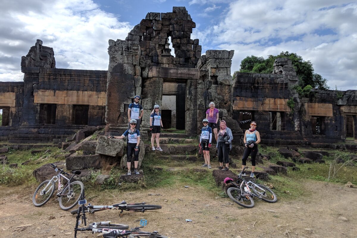 The group standing on the steps of a crumbling stone temple, their bikes lying in front