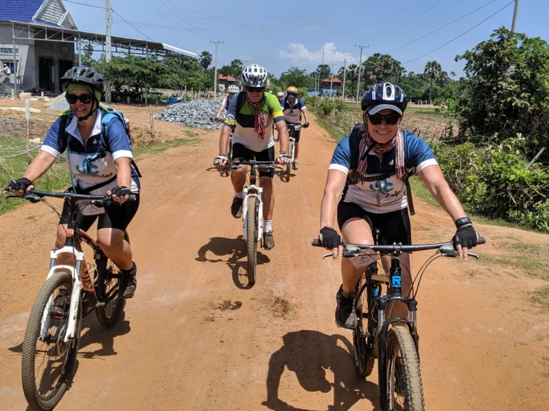 Three cyclists in Social Cycles jerseys riding along a red dirt road in Cambodia