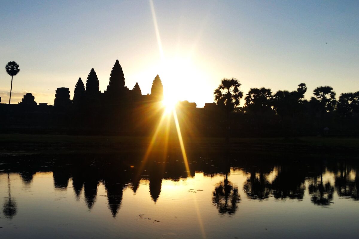 The towers of Angkor Wat silhouetted against the rising sun, reflected in the moat