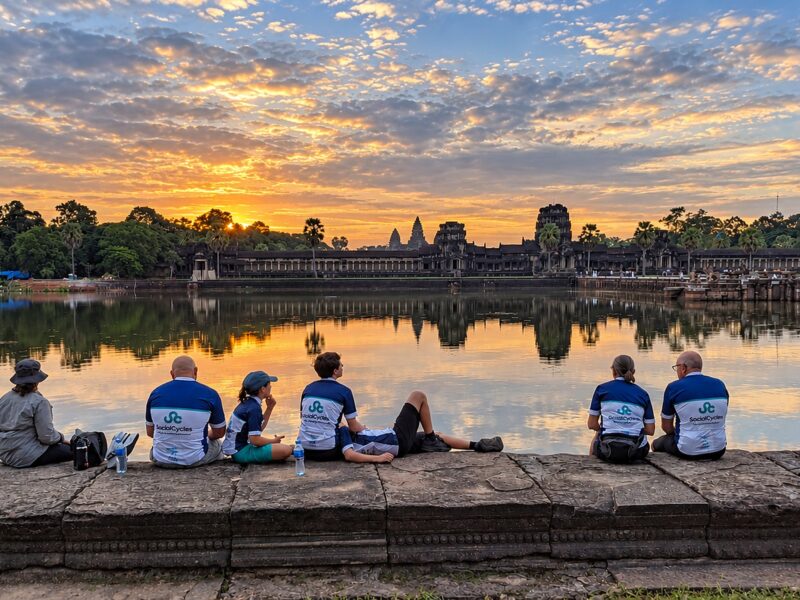 Six riders on the stone edge of the moat at Angkor Wat, watching the sunrise over the temple