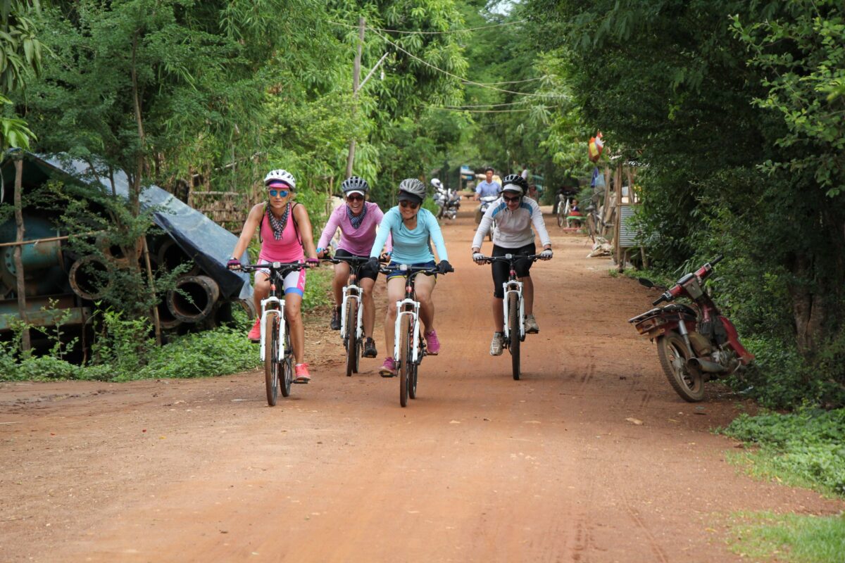 Four riders come down a shaded red village road
