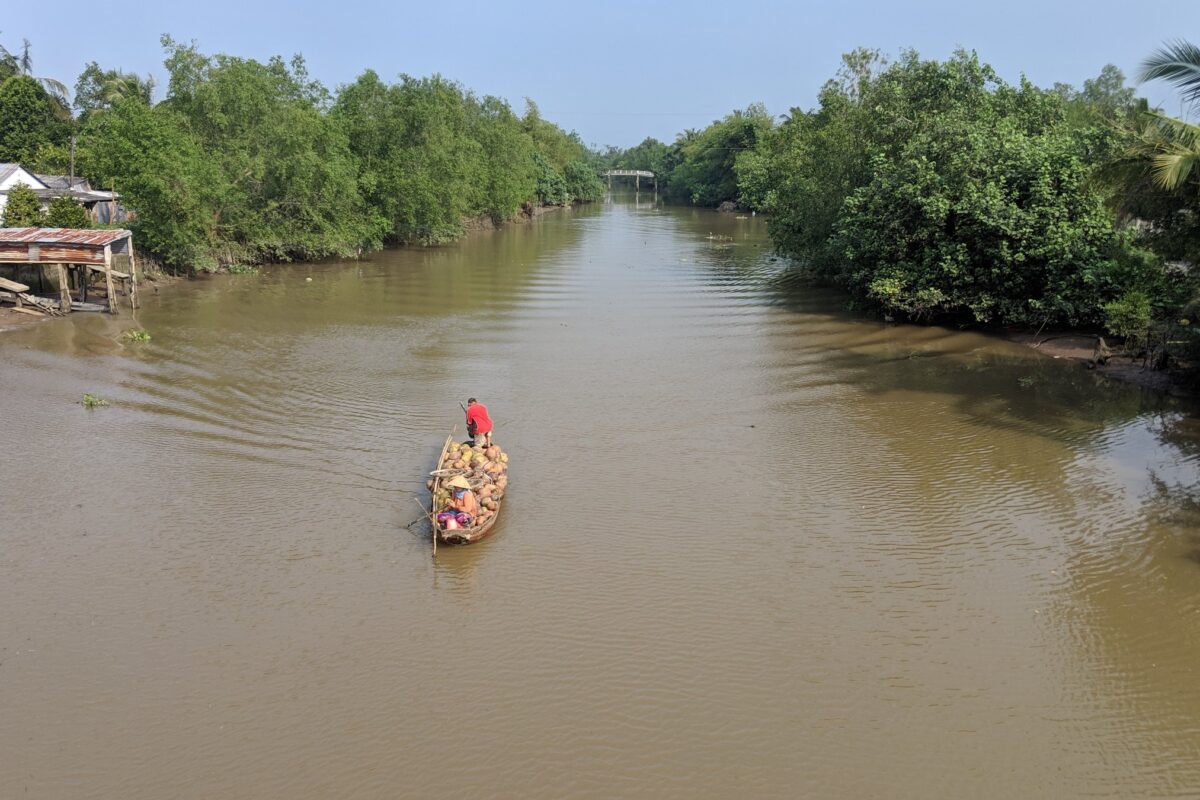 Seen from a bridge, a fruit boat is poled down a wide canal