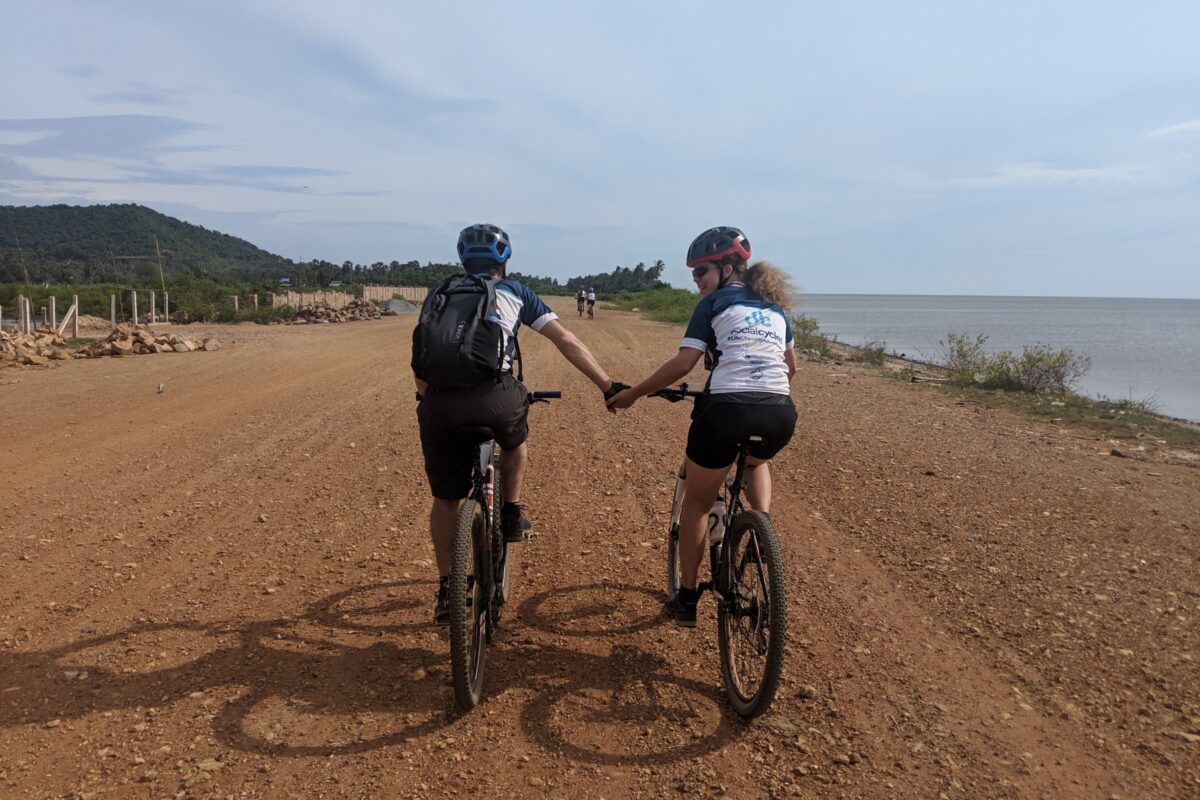 Two riders hold hands along the red coast road by Kep