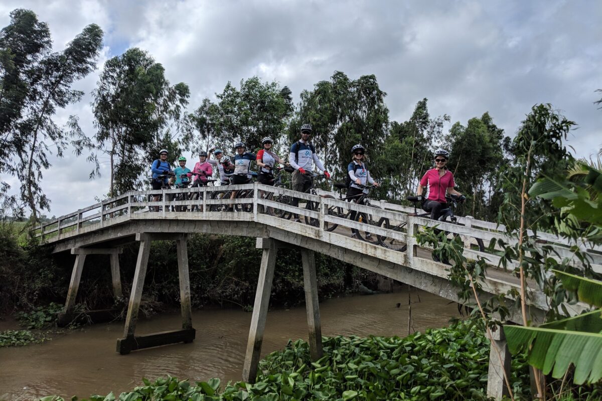 The group with their bikes on a white arched footbridge in the Mekong Delta