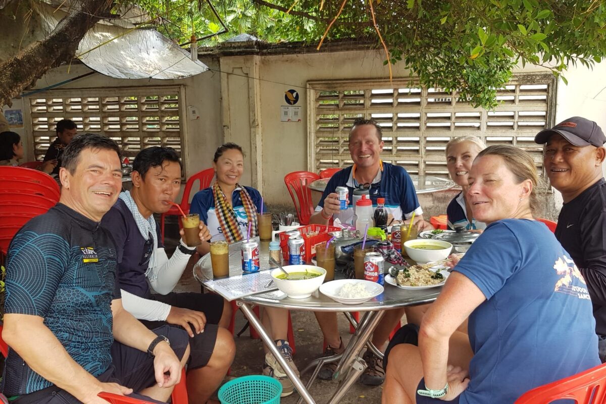 Riders and crew share lunch at a shaded roadside cafe
