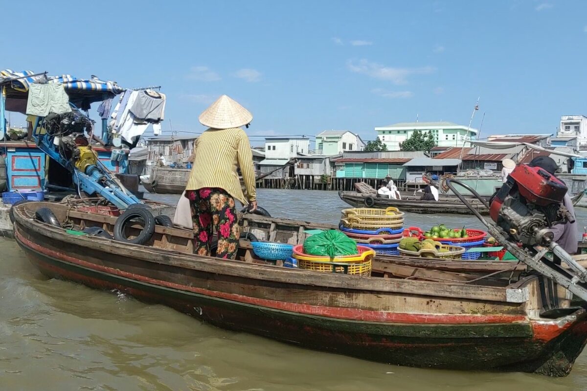 A fruit seller in a conical hat on a boat at the Can Tho floating market
