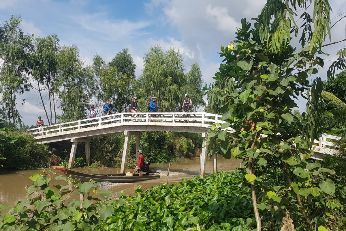 Riders cross an arched bridge as a boatman motors underneath