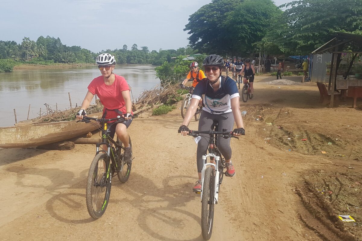 Riders on a riverside track in Battambang, a dugout on the bank