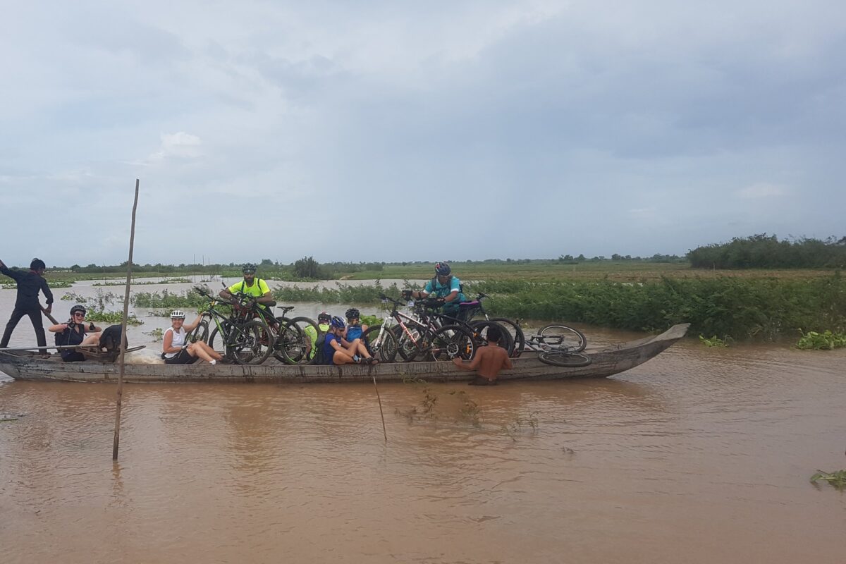 Local boatmen pole a dugout loaded with riders and bikes across flooded fields