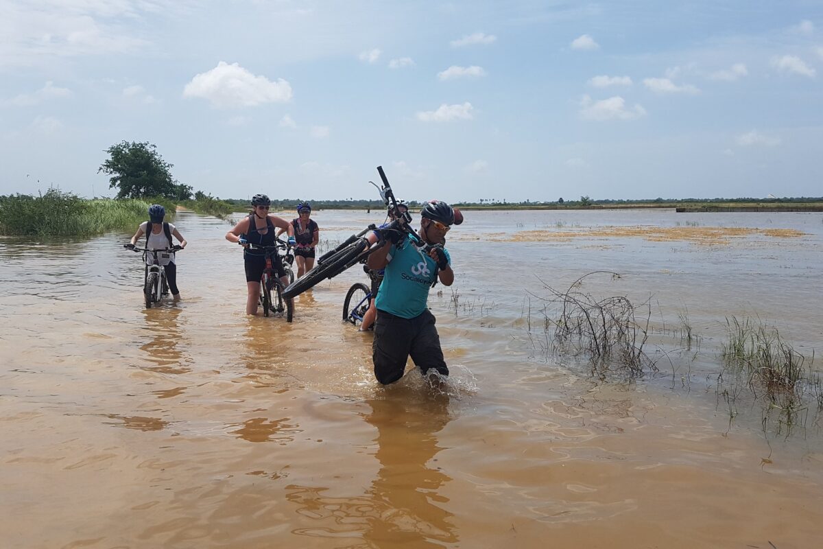 A guide shoulders his bike through the floodwater south of Phnom Penh, riders wading behind