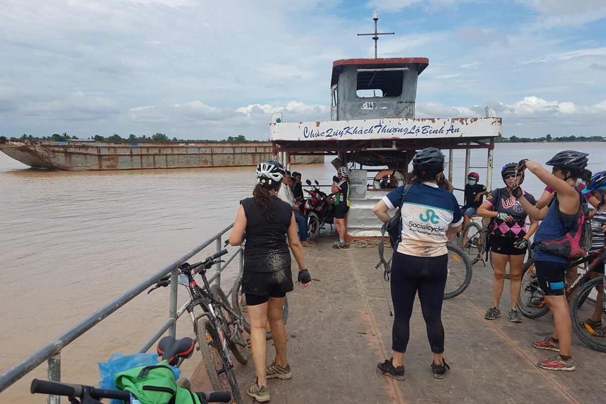 Mud-splashed riders and their bikes on the Mekong ferry