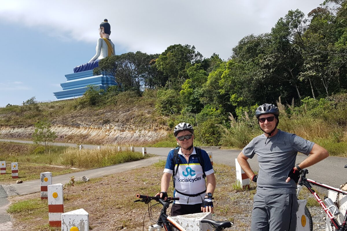 Two riders stop below the giant white Buddha on Bokor mountain