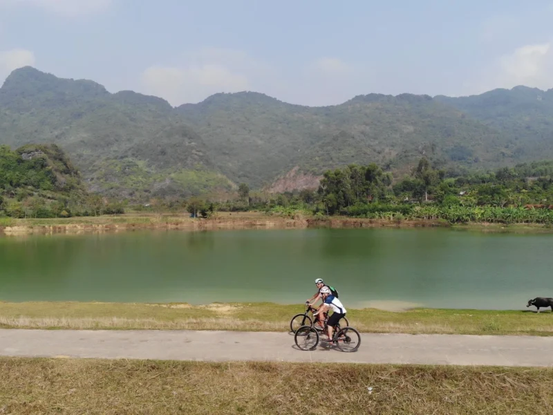 Two riders on a lakeside track below a karst skyline