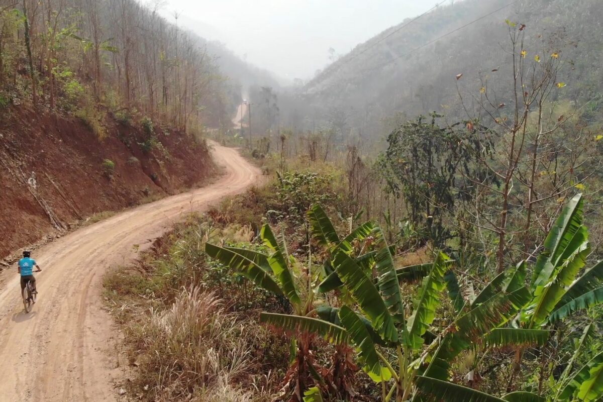 A rider on a winding red-dirt road through dry hills