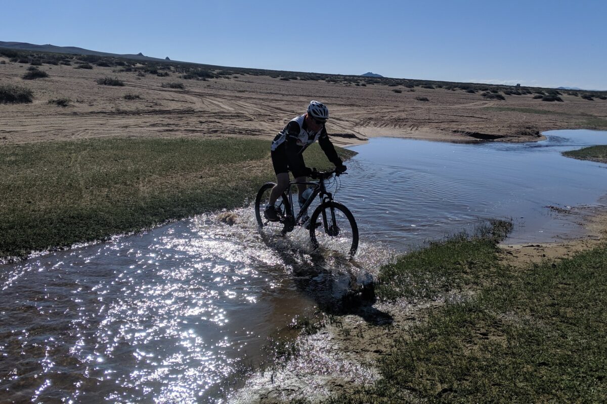 A rider splashes through a sunlit stream on the open steppe